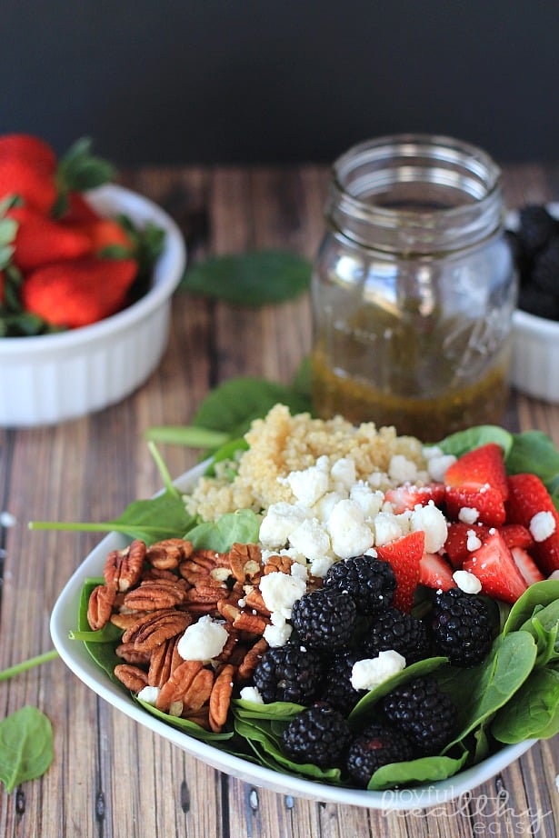 Detox Berry Quinoa Spinach Salad #quinoa #glutenfree #vegetarianrecipes #sidedishes #saladrecipes #summerbbq 排毒浆果藜麦菠菜沙拉放在碗里,旁边是一罐自制的醋汁