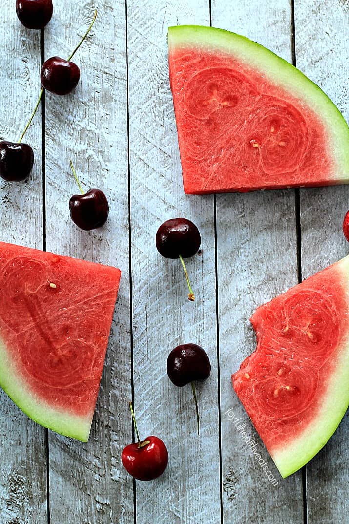 4 Ingredient Cherry Watermelon Granita, a light, sweet, and healthy dessert for the summer! | m.albarakaa.com 西瓜角和新鲜樱桃在木板上的俯视图