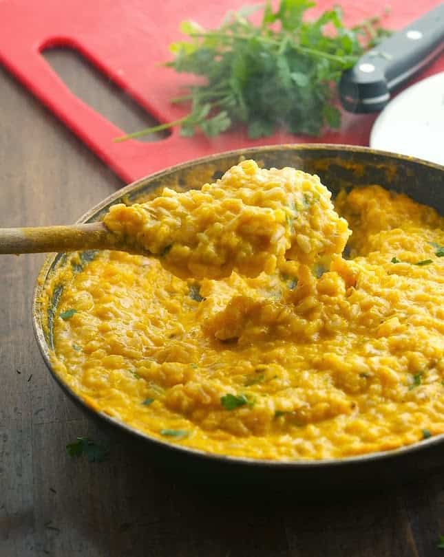 30 of The Best Pumpkin Recipes for Fall 一平底锅装满了奶油南瓜蒜蓉饭,旁边是红色的砧板