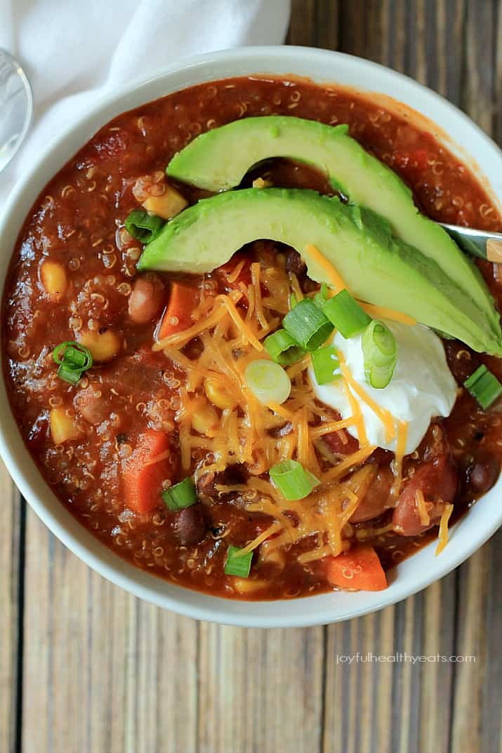 A hearty Quinoa Vegetarian Chili cooked to perfection in the Crock Pot, this soup recipe just screams fall comfort food! |m.albarakaa.com #freezerfriendly #easyrecipes 近距离观看一碗藜麦素食辣椒,上面有葱花、奶酪丝、酸奶油和牛油果片