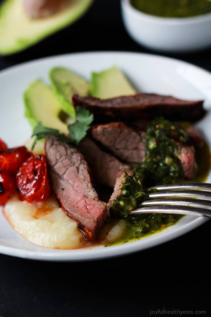 Healthy + Easy Chili Rubbed Flank Steak served with fresh chimichurri sauce, done in 30 minutes. Soooo stinking good! | m.albarakaa.com #recipes #eathealthy #glutenfree 特写:盘子里的辣椒抹牛腩牛排片配上新鲜的墨西哥辣酱、烤西红柿和新鲜的鳄梨