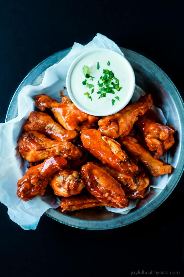 A healthier version of the Classic Buffalo Baked Chicken Wings, these are baked and still have the same crispy sauce taste! | m.albarakaa.com #recipes #appetizer 布法罗烤鸡翅放在盘子里,配上一杯奶油蘸酱