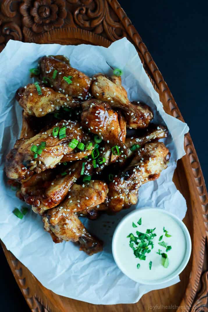 The BEST sauce ever and only for 4 ingredients, this is a must make! Tangy Honey Mustard Baked Chicken Wings | m.albarakaa.com #appetizer #recipes 一堆烤鸡翅放在木托盘上,旁边是一碗蘸酱