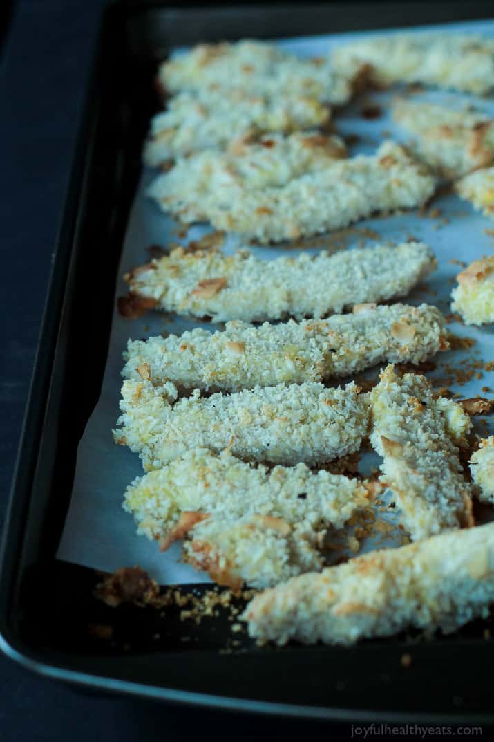 Dinner in 30 minutes! Baked Coconut Crusted Chicken Tenders using just 3 ingredients and served with a Tangy Honey Mustard Sauce for dunking. You will love this! | joyfulhealthyeats.com #recipe 椰子皮鸡柳放在羊皮纸衬里的烤盘上