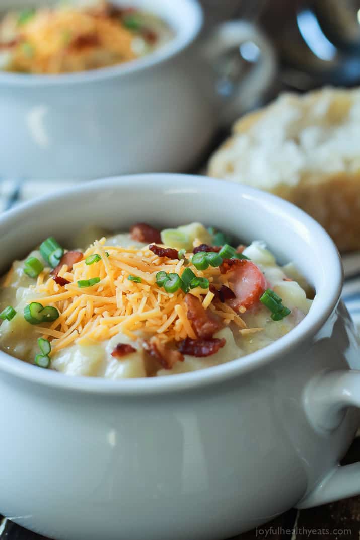 Creamy Potato Leek Soup, the ultimate comfort food soup made healthier with 2% milk, greek yogurt, and extra vegetables. De-lish! | joyfulhealthyeats.com #recipes #glutenfree 特写的奶油土豆韭菜汤在一个瓦罐,上面有碎奶酪,葱和培根