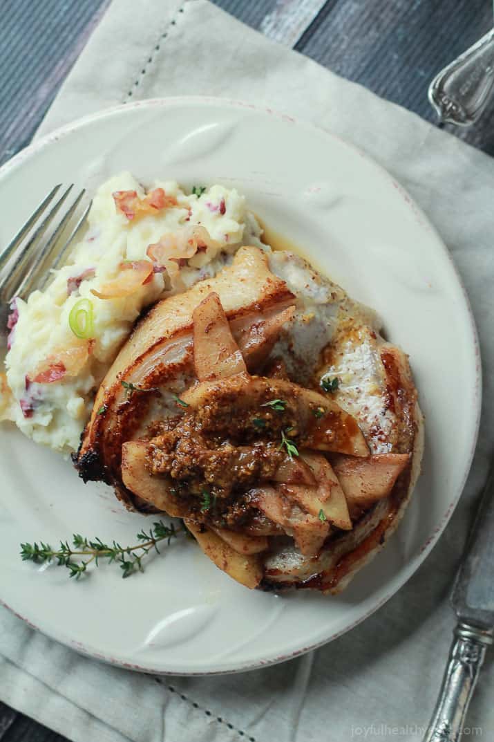 Mustard Crusted Pork Chops with Bourbon Glazed Apples 一盘猪肉和釉面苹果在侧面有装载的土豆泥