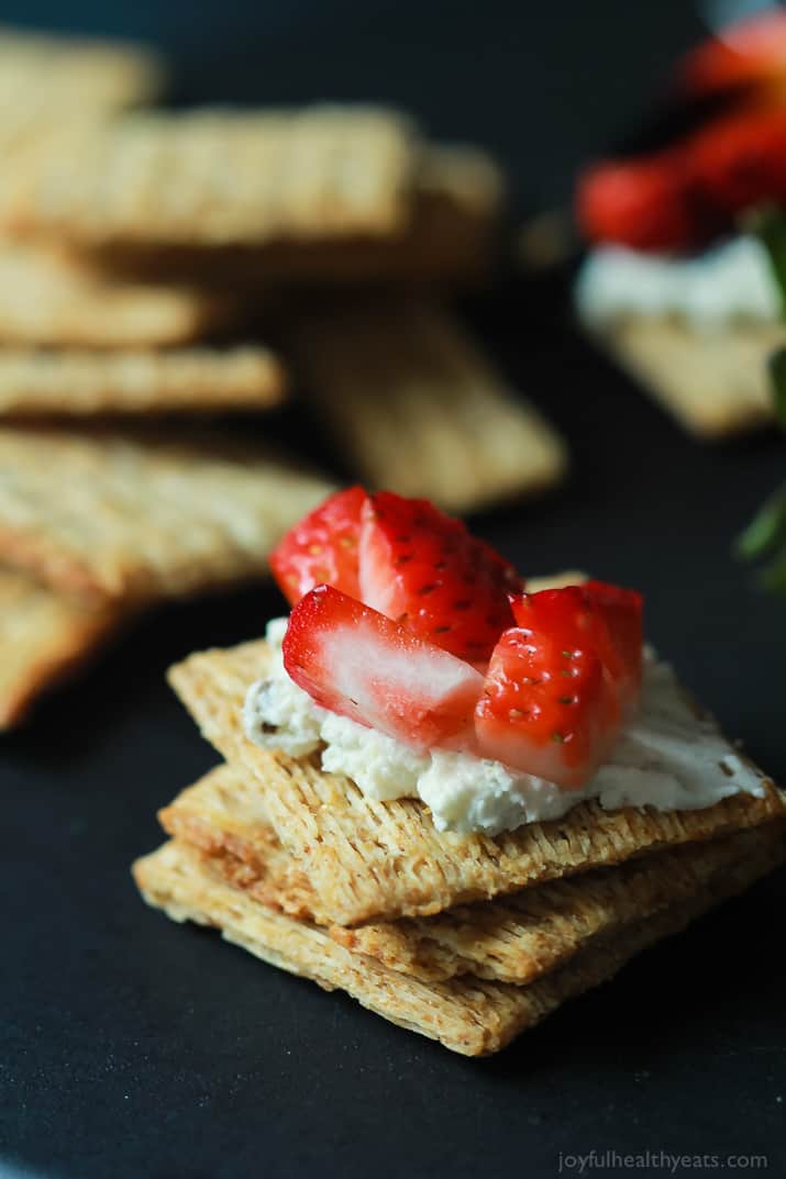 An easy spring party appetizer using less than 5 ingredients! Strawberry Goat Cheese Bites topped with a Balsamic Reduction Drizzle, takes only five minutes to make! | joyfulhealthyeats.com #recipes #appetizer #ad 一堆饼干上面有山羊奶酪和草莓丁