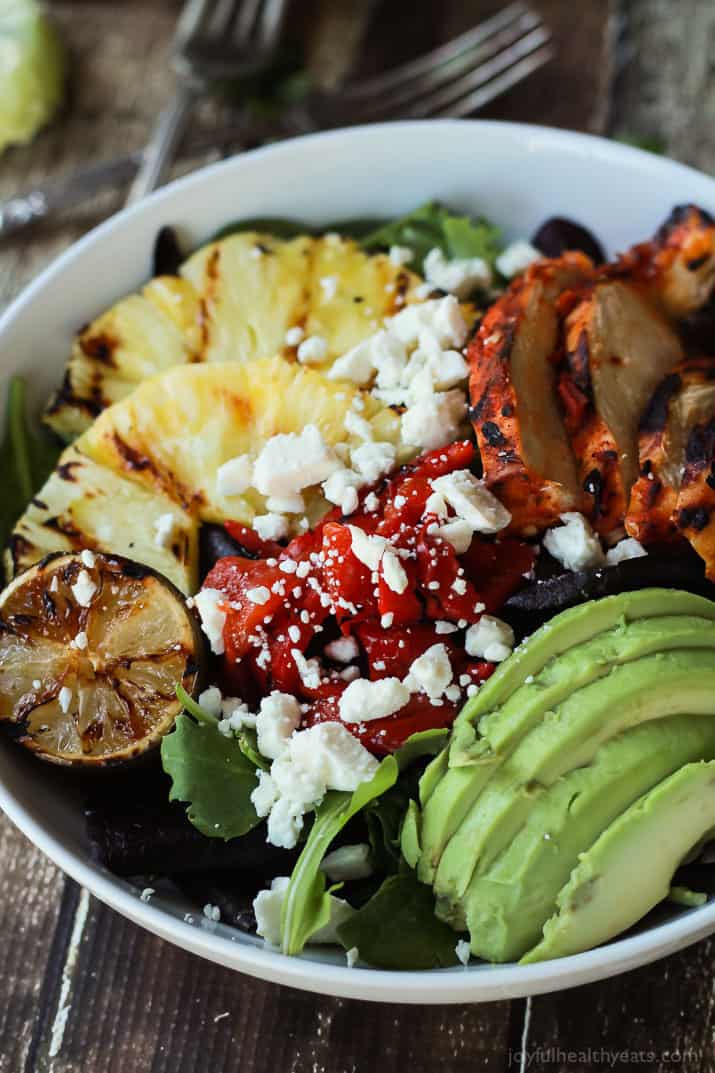 Harissa Lime Grilled Chicken Salad with a Creamy Cilantro Lime Vinaigrette, filled with grilled pineapple, limes, fresh avocado and an amazing dressing! Add to your list! | joyfulhealthyeats.com #glutenfree #recipes Harissa Lime Grilled Chicken Salad in a bowl with grilled pineapple, roasted red pepper, sliced avocado and crumbled feta