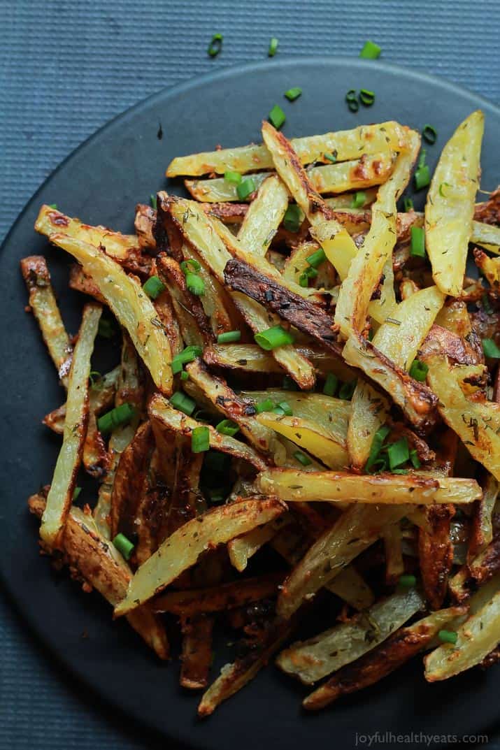 Crispy Baked Garlic Parmesan Fries are crispy on the outside and soft on the inside, the easiest skinny Baked Fries you will ever make! Only 6 ingredients but pack a phenomenal fresh herb taste! | joyfulhealthyeats.com #recipes #glutenfree 顶视图的脆蒜帕尔马干酪薯条与大葱在一盘