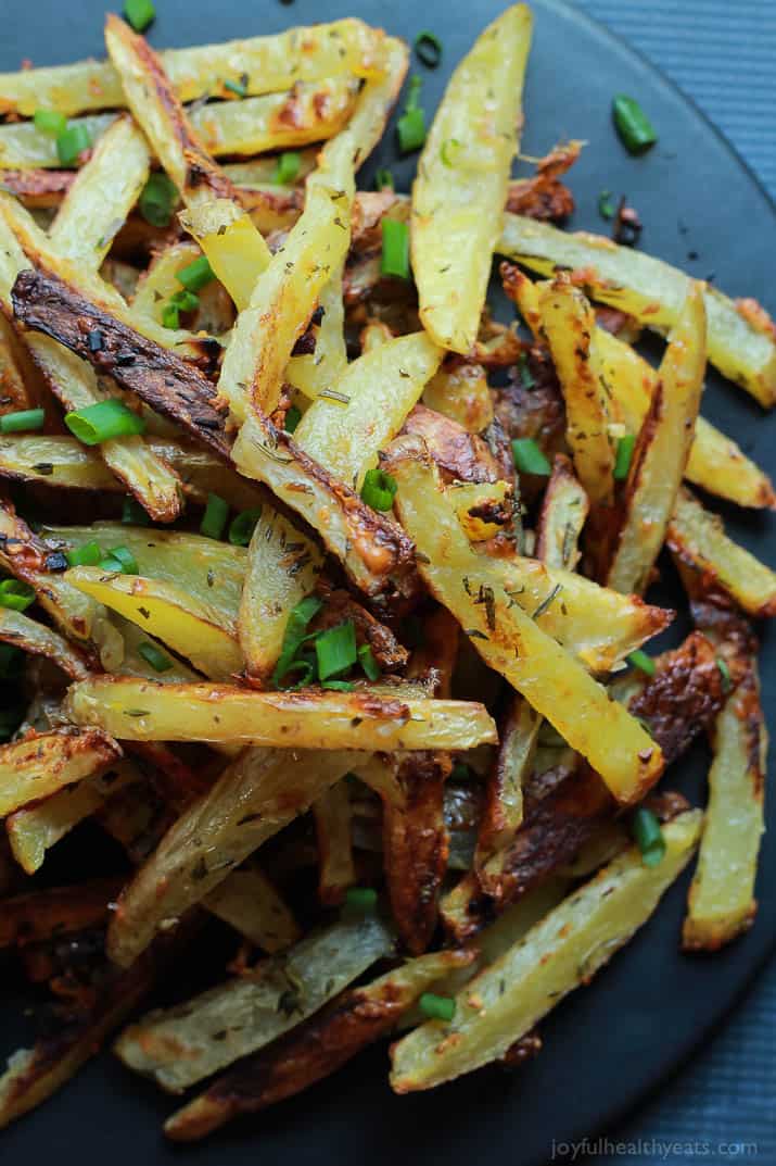 Crispy Baked Garlic Parmesan Fries are crispy on the outside and soft on the inside, the easiest skinny Baked Fries you will ever make! Only 6 ingredients but pack a phenomenal fresh herb taste! | joyfulhealthyeats.com #recipes #glutenfree 顶视图的脆蒜帕尔马干酪薯条与大葱在一盘