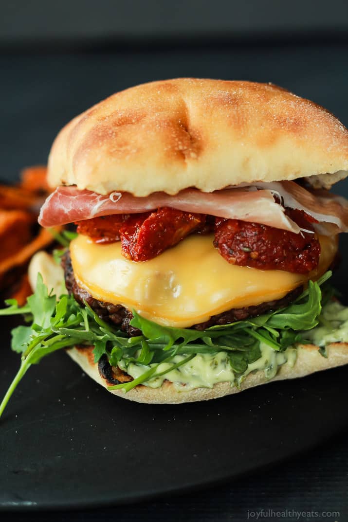 A juicy Italian Cheeseburger served on a toasted ciabatta bun, topped with smoked gouda cheese, spicy arugula, sun dried tomatoes, salty prosciutto, and basil pesto aioli! Done in 15 minutes this Burger is sure to be your new favorite this summer! | joyfulhealthyeats.com #recipes #grill #easy 一个多汁的意大利芝士汉堡配上烤过的夏巴塔面包,上面有熏豪达奶酪、辣芝麻菜、晒干的番茄、咸熏火腿和罗勒香蒜沙蒜泥蛋黄酱!只要15分钟,这个汉堡一定会成为你今夏的新宠!| joyfulhealthyeats.com #食谱#烧烤#简单