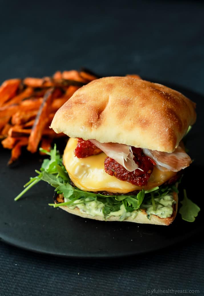 A juicy Italian Cheeseburger served on a toasted ciabatta bun, topped with smoked gouda cheese, spicy arugula, sun dried tomatoes, salty prosciutto, and basil pesto aioli! Done in 15 minutes this Burger is sure to be your new favorite this summer! | joyfulhealthyeats.com #recipes #grill #easy 一个多汁的意大利芝士汉堡配上烤过的夏巴塔面包,上面有熏豪达奶酪、辣芝麻菜、晒干的番茄、咸熏火腿和罗勒香蒜沙蒜泥蛋黄酱!只要15分钟,这个汉堡一定会成为你今夏的新宠!| joyfulhealthyeats.com #食谱#烧烤#简单
