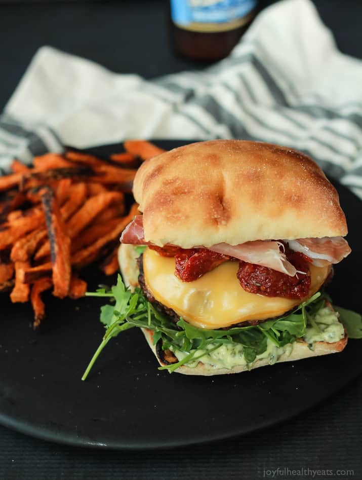 A juicy Italian Cheeseburger served on a toasted ciabatta bun, topped with smoked gouda cheese, spicy arugula, sun dried tomatoes, salty prosciutto, and basil pesto aioli! Done in 15 minutes this Burger is sure to be your new favorite this summer! | joyfulhealthyeats.com #recipes #grill #easy 一个多汁的意大利芝士汉堡配上烤过的夏巴塔面包,上面有熏豪达奶酪、辣芝麻菜、晒干的番茄、咸熏火腿和罗勒香蒜沙蒜泥蛋黄酱!只要15分钟,这个汉堡一定会成为你今夏的新宠!| joyfulhealthyeats.com #食谱#烧烤#简单