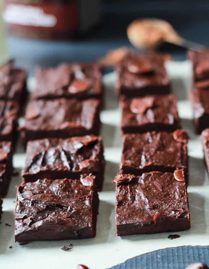 The Best Fudgy Avocado Brownies you will ever taste, packed with coconut sugar, chocolate chips, and coffee! The perfect guilt free dessert recipe for the summer! | joyfulhealthyeats.com #recipes Fudgy Avocado Brownies on parchment cut into squares