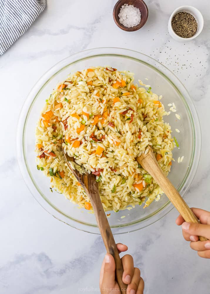 Mediterranean Orzo Pasta Salad 两只手在一碗意大利面沙拉里舀木勺