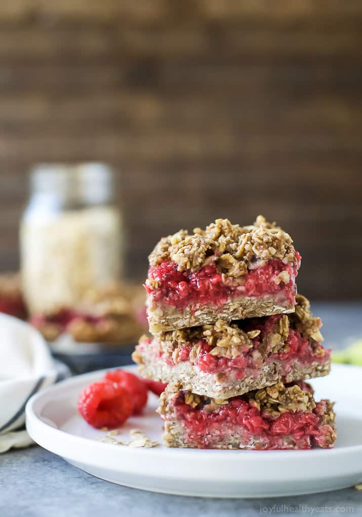 Almond Oat Raspberry Bar Recipe 三根覆盆子棒和一些松散的浆果堆叠在盘子上