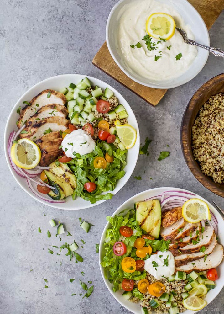 Top view of two Chicken Shawarma Bowls on a bed of quinoa and lettuce next to a bowl of Garlic Yogurt Sauce
