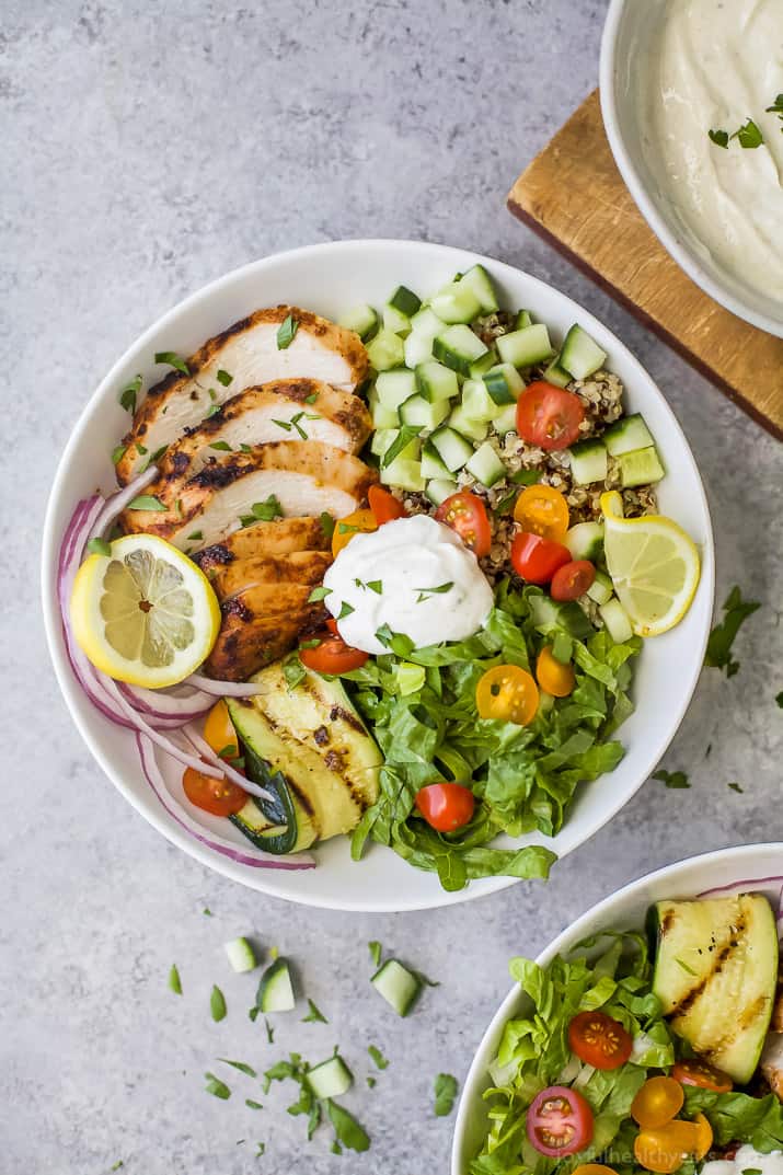 Top view of a Chicken Shawarma Bowl on a bed of quinoa and lettuce and topped with diced veggies and Garlic Yogurt Sauce