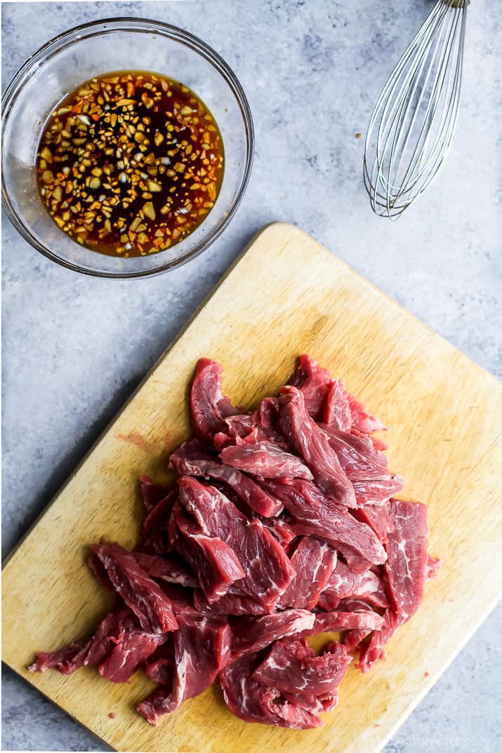 在一个切板的未加工的切的牛肉旁边一碗甜辣韩国酱汁