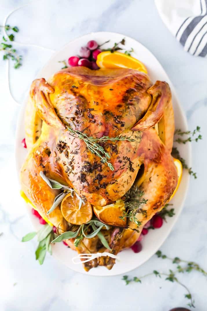 The Best Thanksgiving Turkey Recipe without Brining Cooked Thanksgiving turkey on a white platter garnished with cranberries and herbs