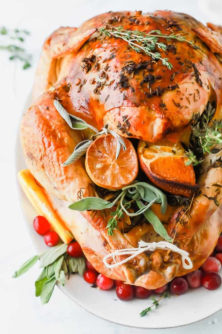 The Best Thanksgiving Turkey Recipe without Brining Roasted turkey on a white platter stuffed with orange slices and herbs