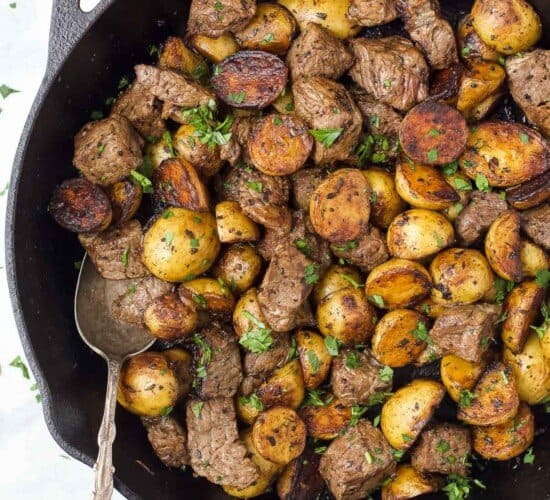 大蒜黄油牛排和小土豆放在平底锅里,用金属勺子