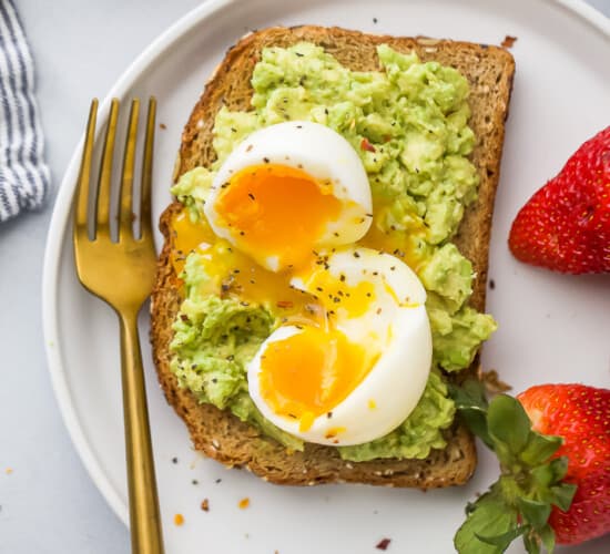 特写镜头顶上的视图的粉碎的鲕梨吐司顶上与一个软的煮沸的鸡蛋配用新鲜的草莓