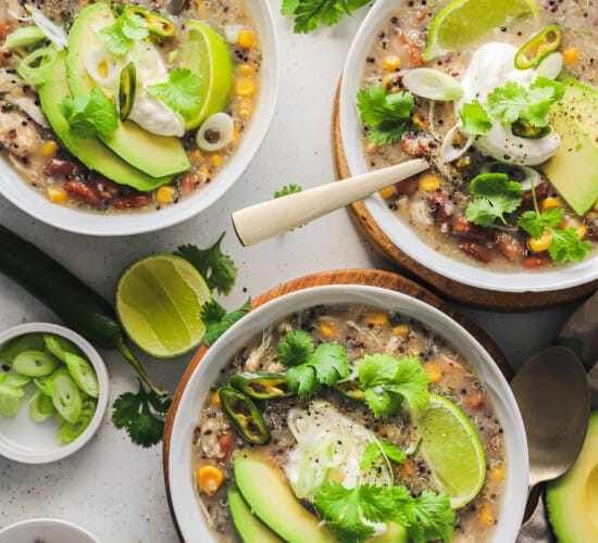 Three bowls on a countertop containing white chicken chili with spoons inside two of them