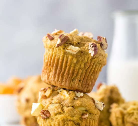 Two apple pecan muffins stacked on top of one another with a glass of milk behind them