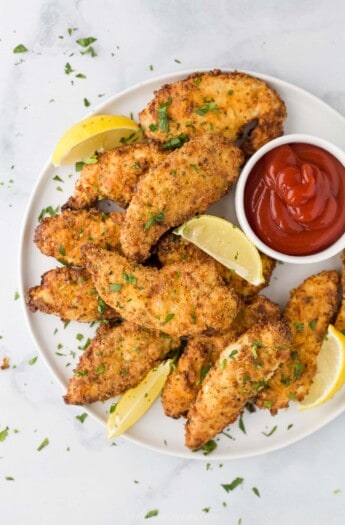 空气炸锅chicken strips on a plate with fresh lemon slices and ketchup