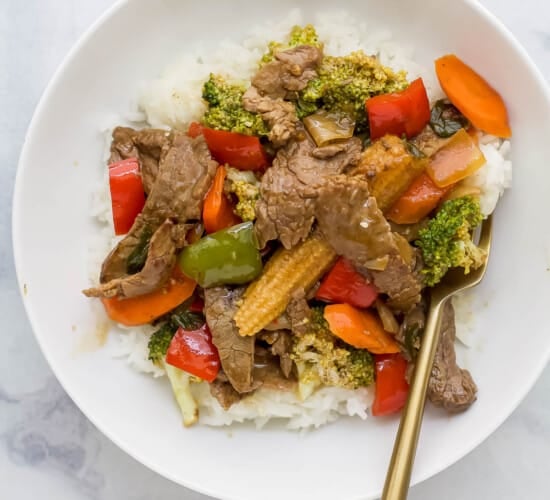牛肉和蔬菜拌在米饭上，放在白色的盘子里